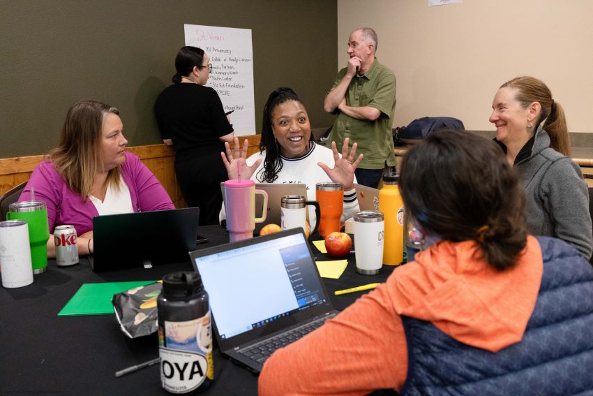 School leaders seated at a table with laptops discussing Family School and Community Partnerships.