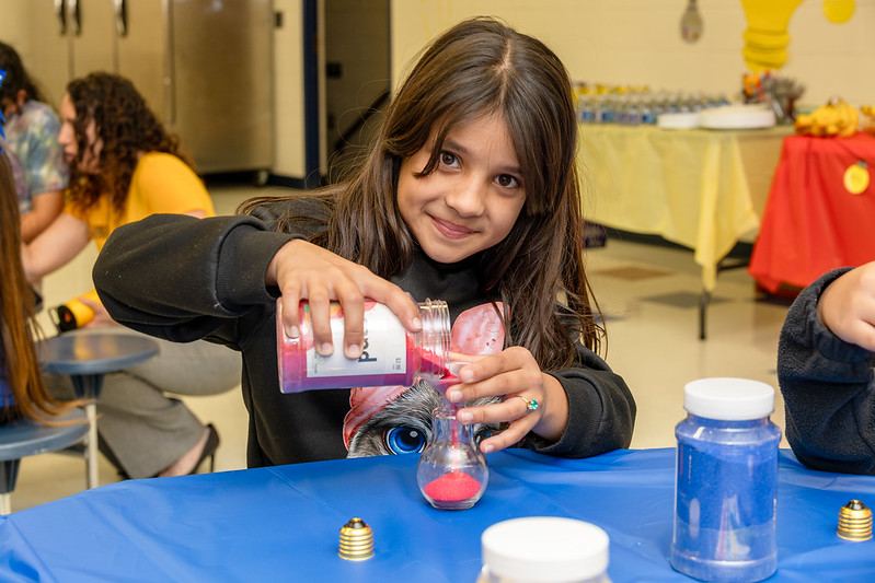 A girl pours red sand into a lightbulb. 