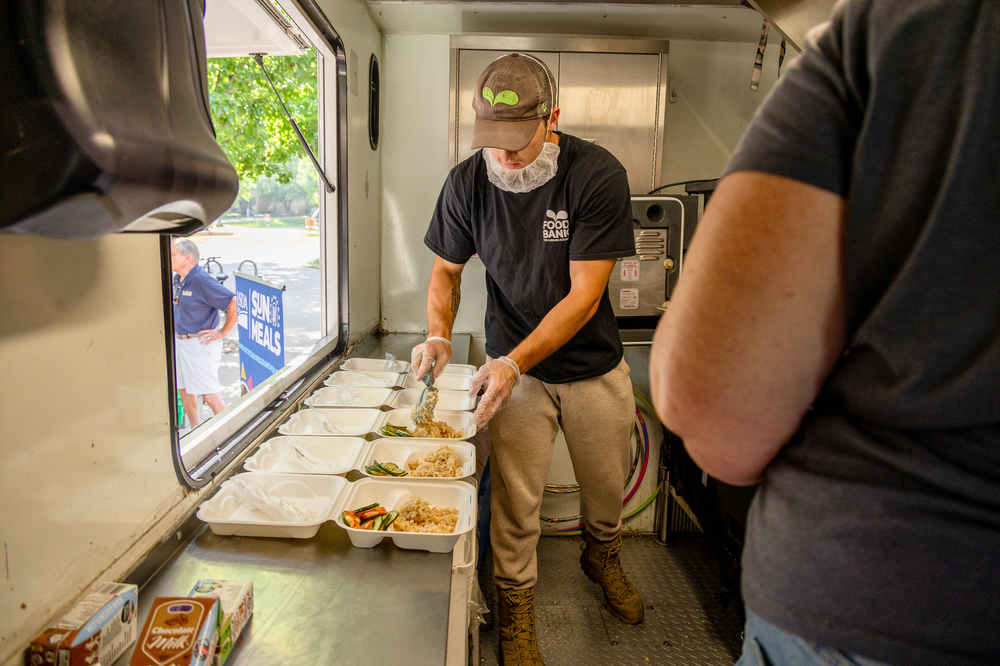 A man on a food truck adds a scoop of rice to a take away box. 