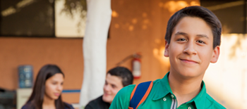 Boy smiling while outside of school building, other students talking in background