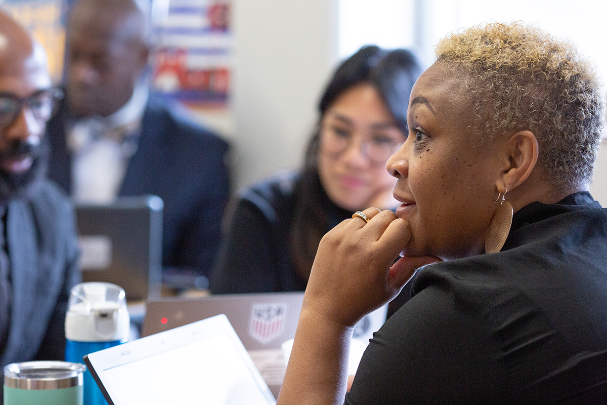 Group of adults sitting at a table, business setting, focus is on a woman who is alert and engaged